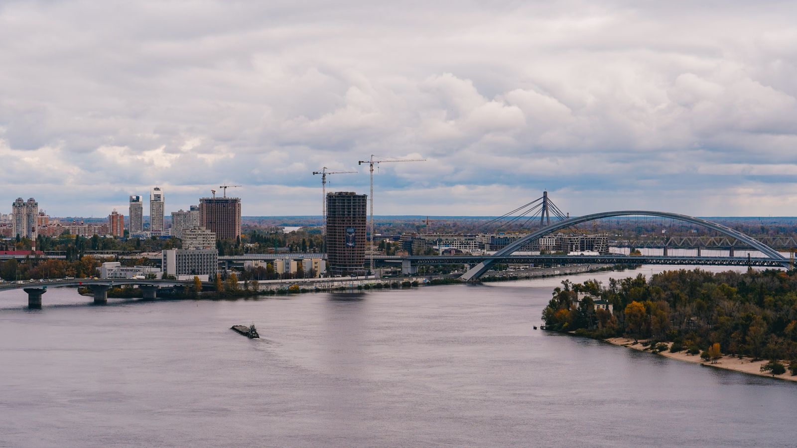 River, bridges, and skyline in Kyiv under a cloudy sky.