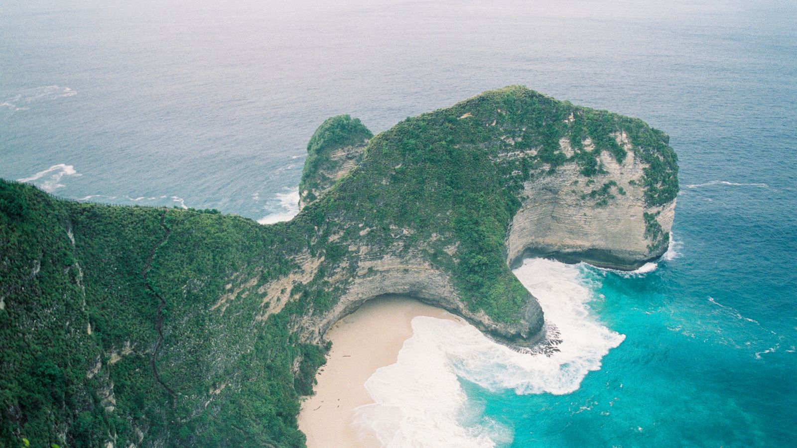 Aerial view of Kelingking Beach limestone cliffs and turquoise water on Nusa Penida, Bali.