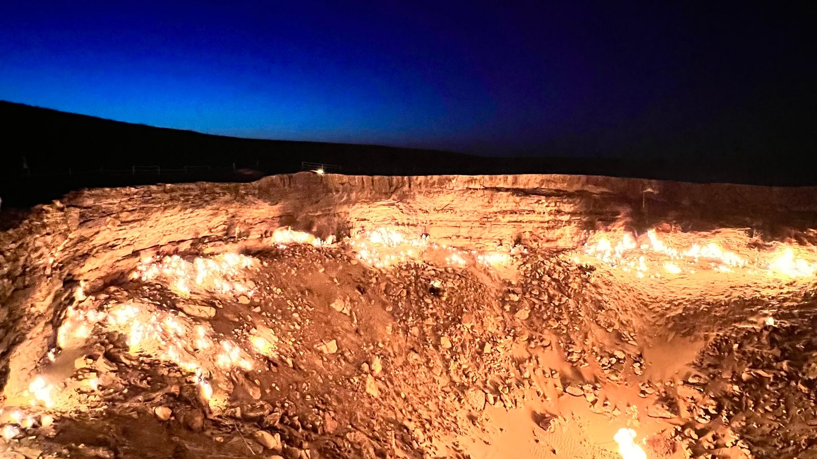 Night view of the Darvaza gas crater in Turkmenistan, with many flames along the rocky pit.