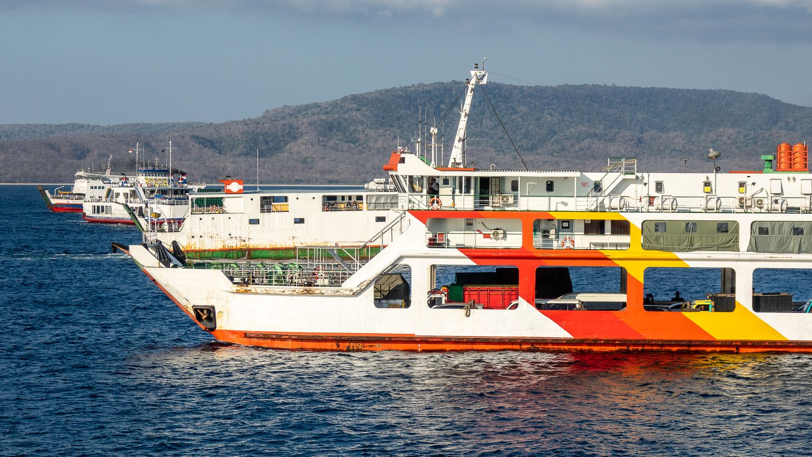Ferries on blue water beside a forested Indonesian coast near Bali.