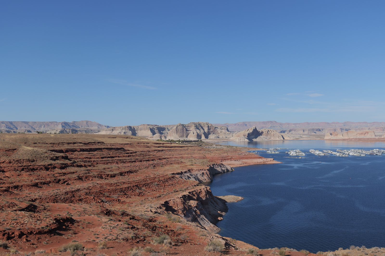 Red rock cliffs meet a canyon reservoir with small boats on the water.