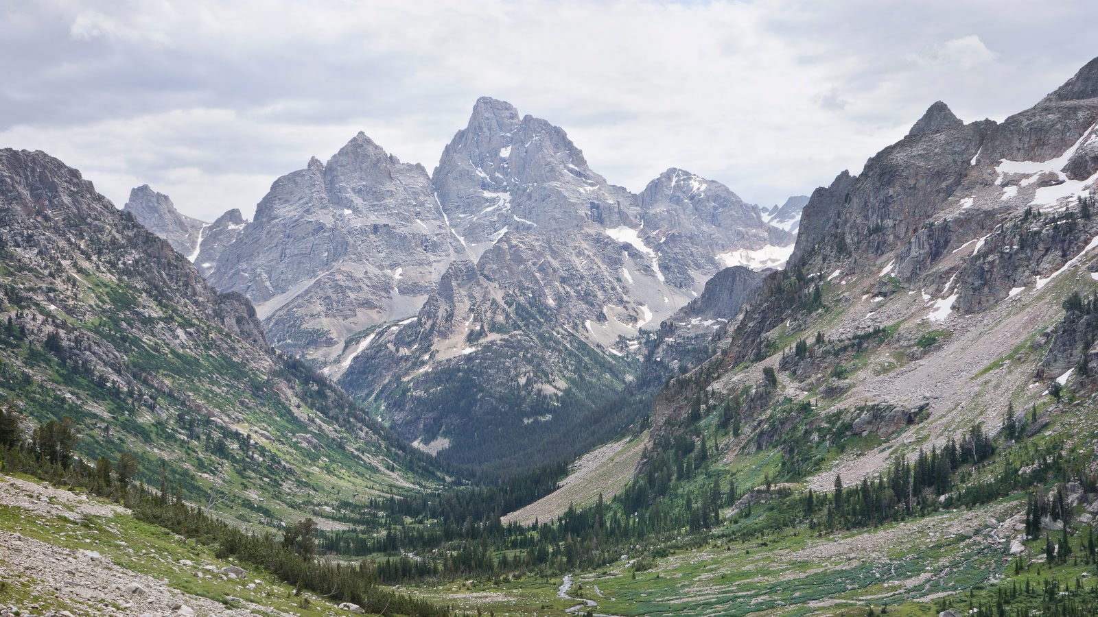 Jagged Grand Teton peaks rise above a green valley and alpine stream.