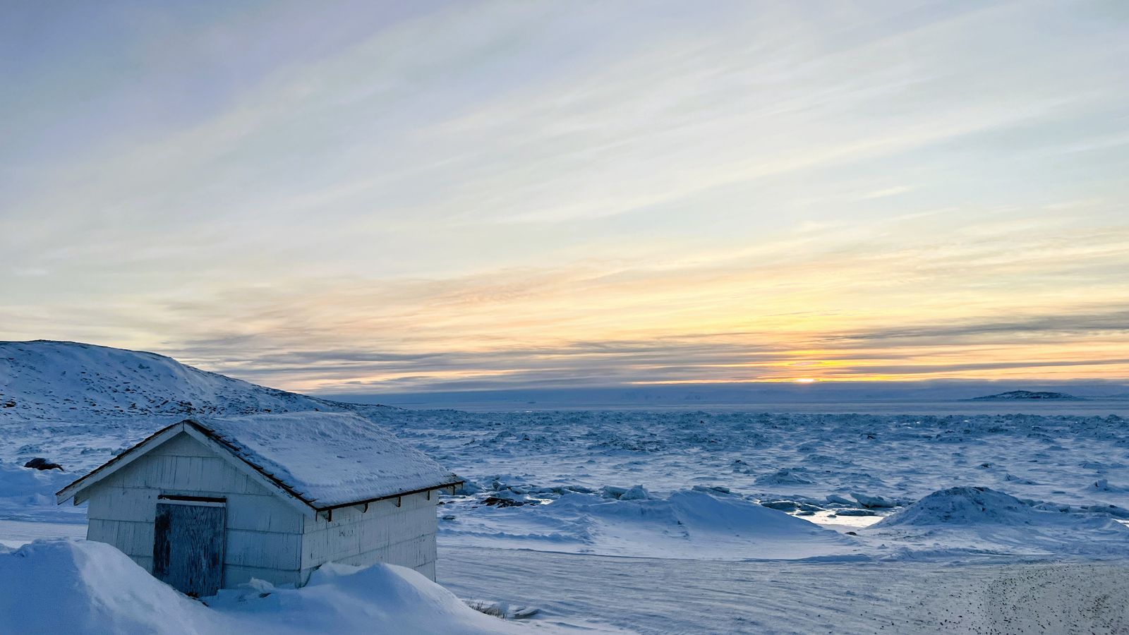 Snow-covered cabin and frozen sea at sunset in Apex, Nunavut.