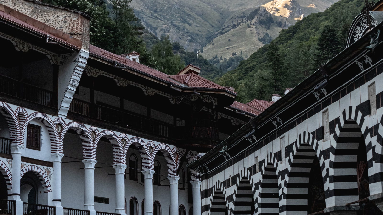 Rila Monastery courtyard arches open toward forested Bulgarian mountains.
