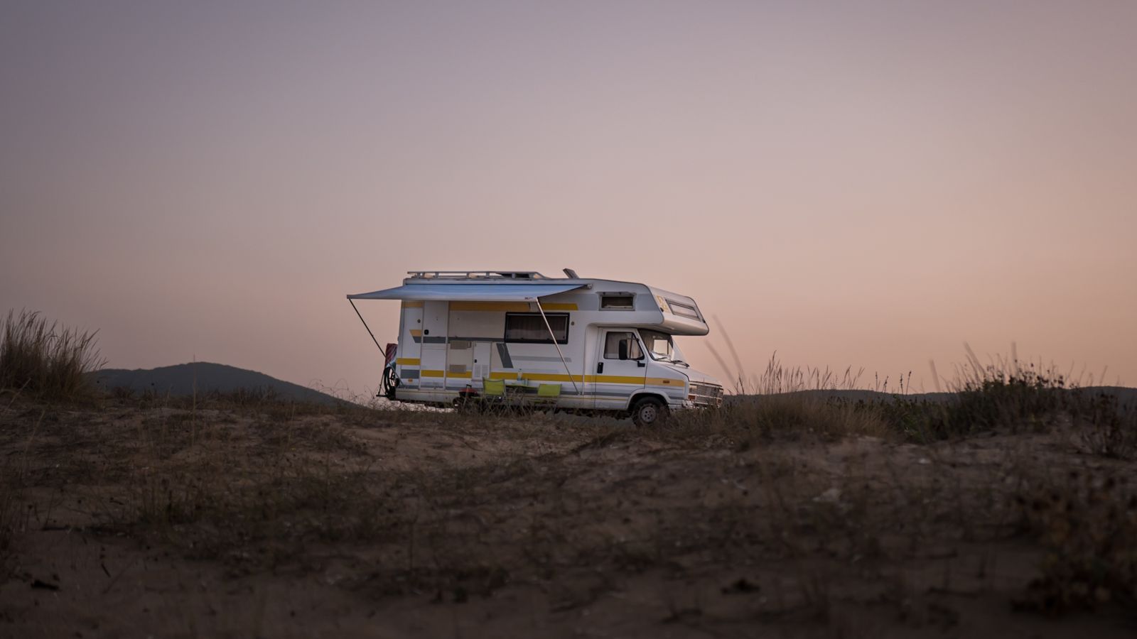A camper van parked on open ground at dusk.