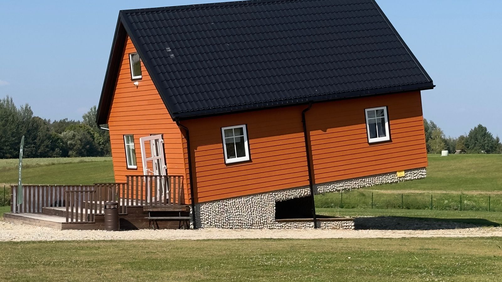 A wooden house built at a steep tilt in an open field.