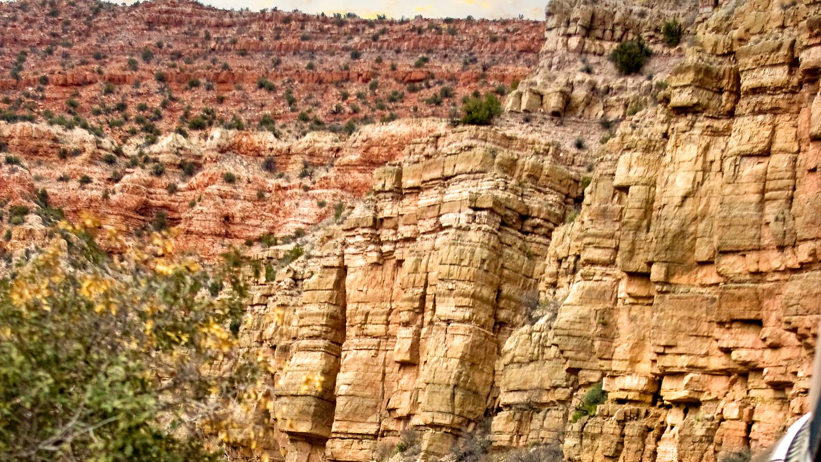 A passenger train follows the track through a red rock canyon.