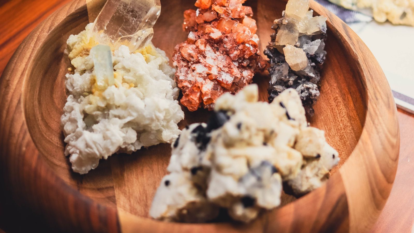 Raw mineral specimens in a wooden bowl.