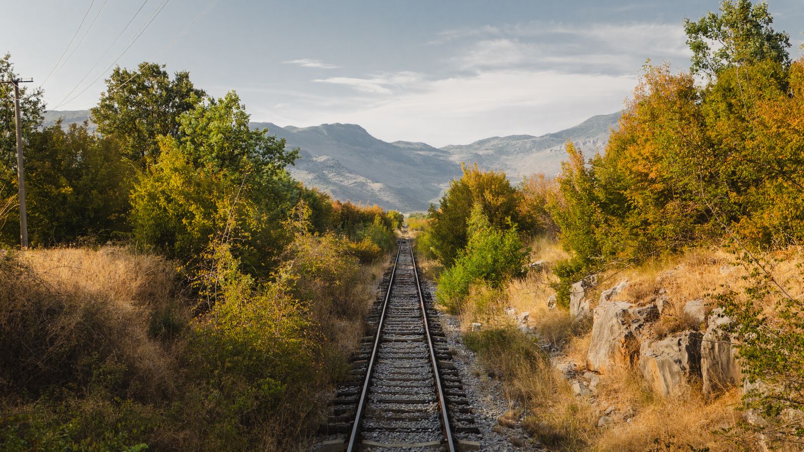 Railway tracks through autumn hills toward mountains in Montenegro.