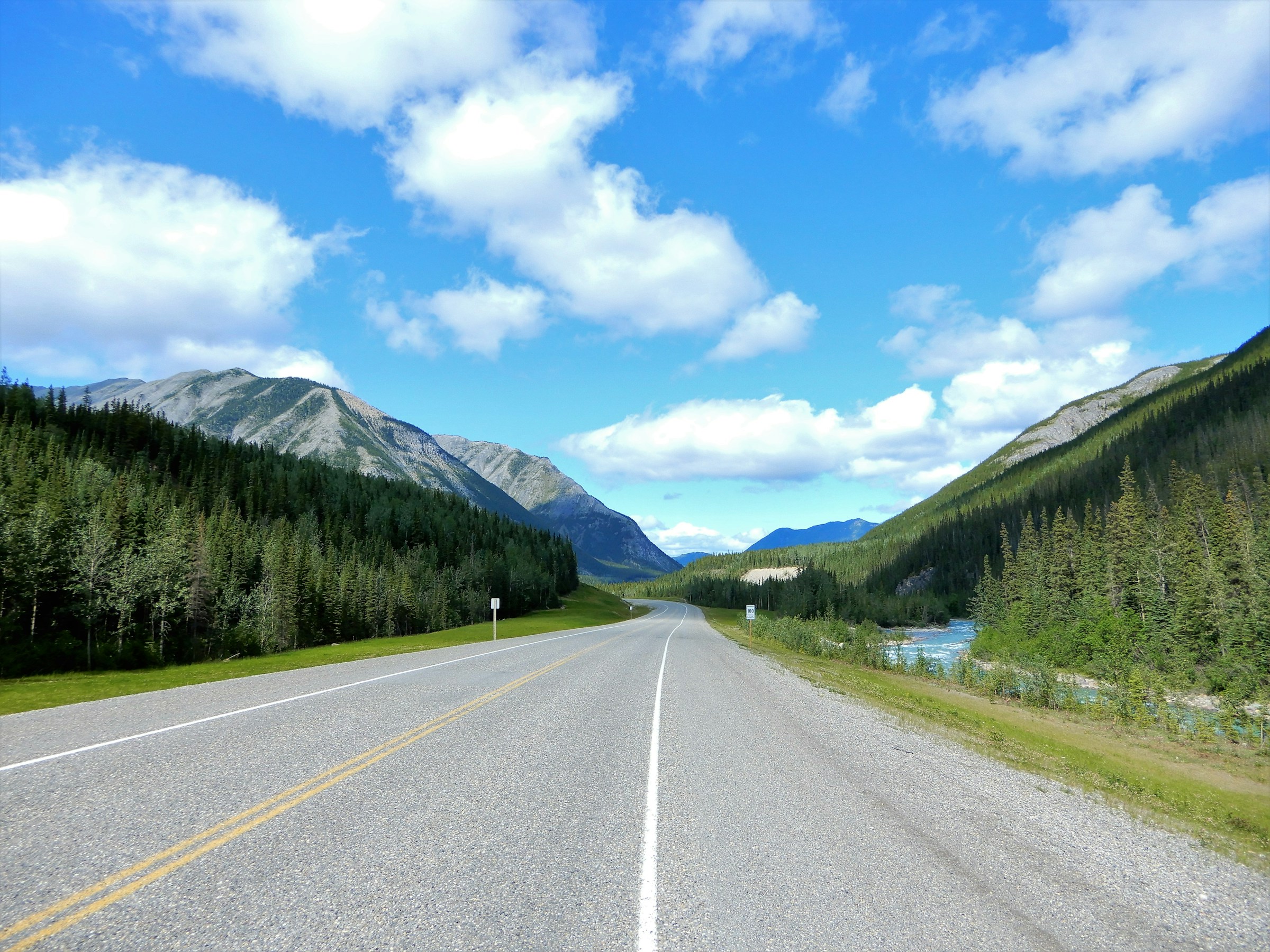 Empty two-lane Alaska highway under mountains in summer light, road-trip planning mood